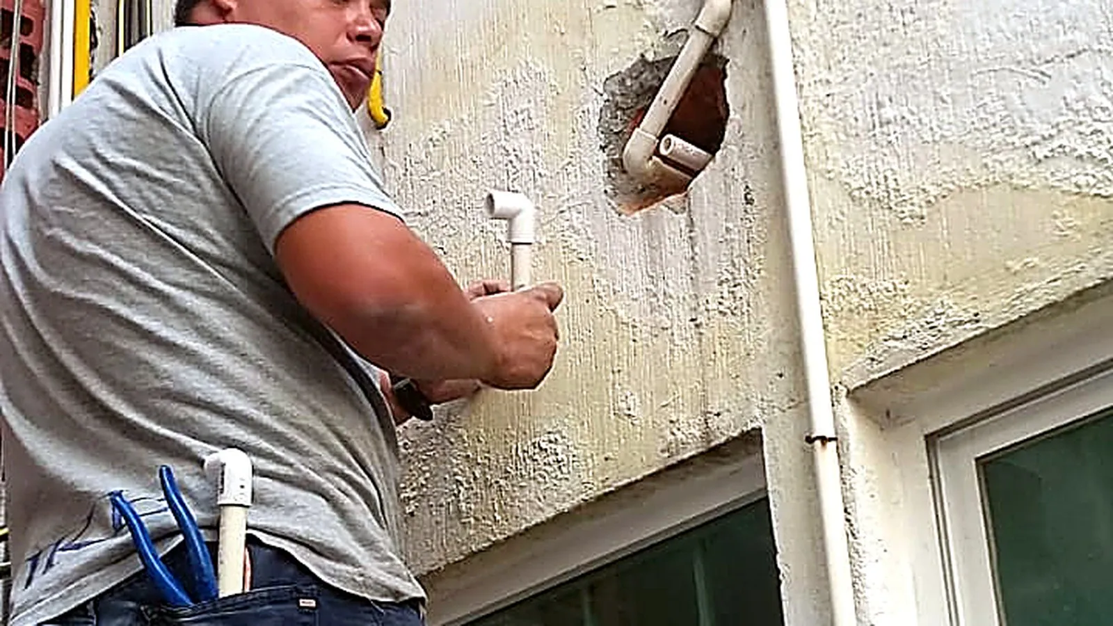 Plomero reparando tubería de agua en pared exterior para eliminar fugas en CDMX